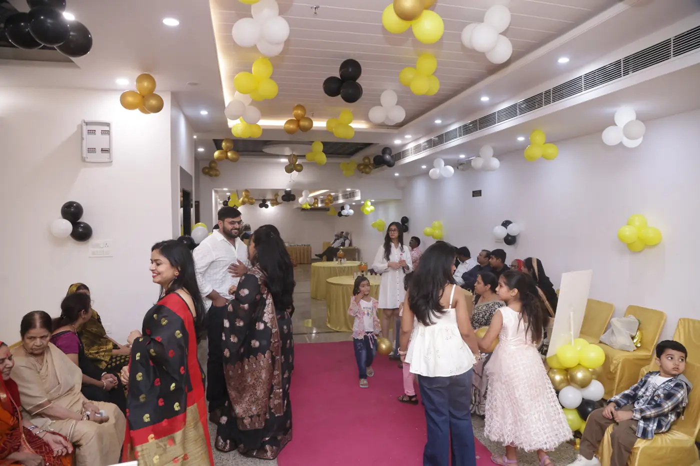 Guests gathered in a hall decorated with yellow, black and white balloons