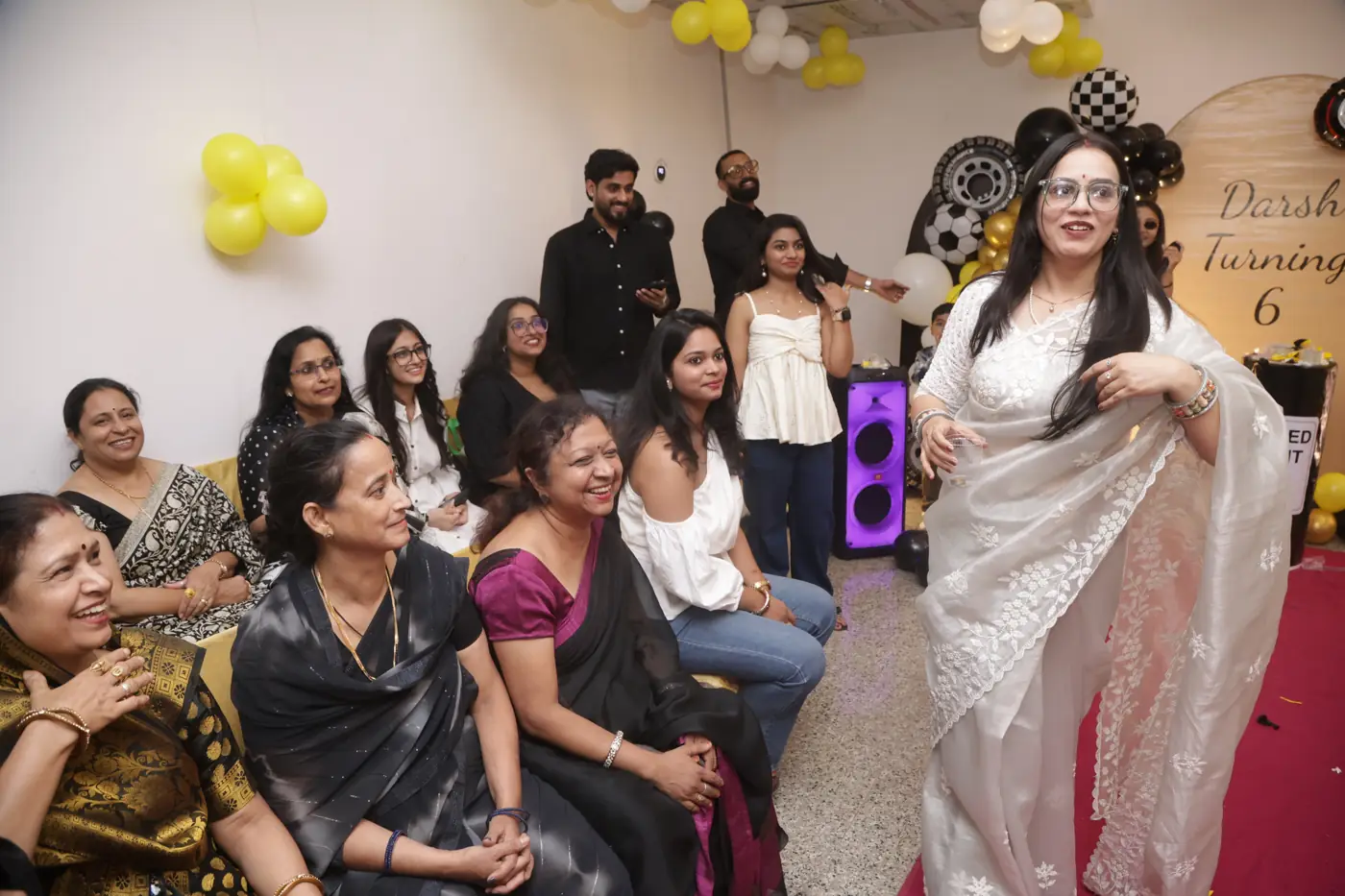 A guest in a white saree singing while others watch